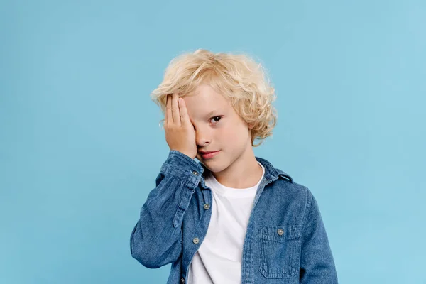 Tired and cute kid obscuring face isolated on blue — Stock Photo