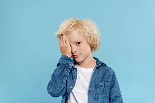 Müde und niedliche Kind verdeckt Gesicht isoliert auf blau — Stockfoto