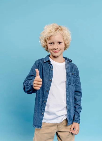 Sonriente y lindo niño mirando a la cámara y mostrando como aislado en azul - foto de stock