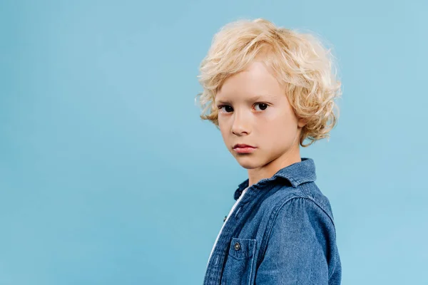Симпатичный и блондинка ребенок смотрит на камеру изолированный на голубом — стоковое фото