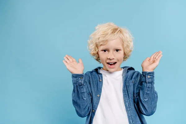 Bambino sorridente e scioccato con le mani tese guardando la fotocamera isolata sul blu — Foto stock