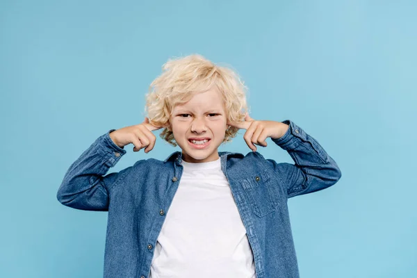 Irritated and cute kid looking at camera and touching ears isolated on blue — Stock Photo