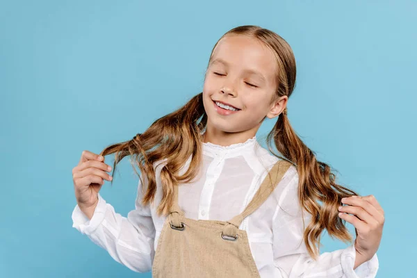 Sorridente e bonito criança tocando cabelo isolado no azul — Fotografia de Stock