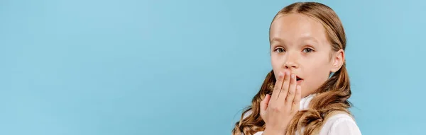 Panoramic shot of shocked and cute kid looking at camera and obscuring face isolated on blue — Stock Photo