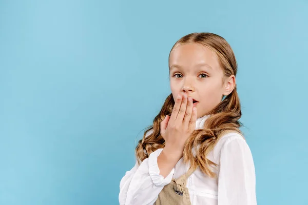 Schockiertes und nettes Kind, das in die Kamera schaut und sein Gesicht verdeckt, isoliert auf blauem Grund — Stockfoto