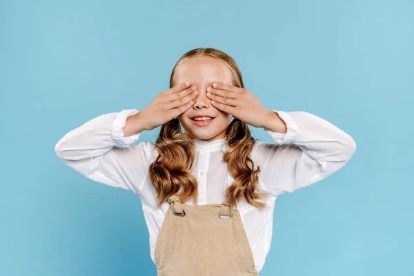 Sorridente e bonito criança obscurecendo rosto isolado no azul — Fotografia de Stock