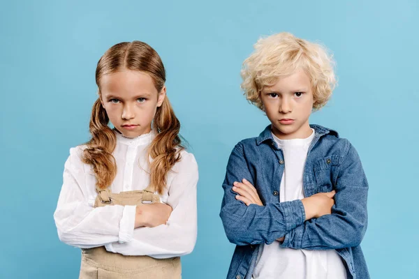 Crianças tristes e bonitos com braços cruzados olhando para a câmera isolada no azul — Fotografia de Stock