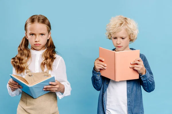 Bambini tristi e carini guardando la fotocamera e leggendo libro isolato sul blu — Foto stock