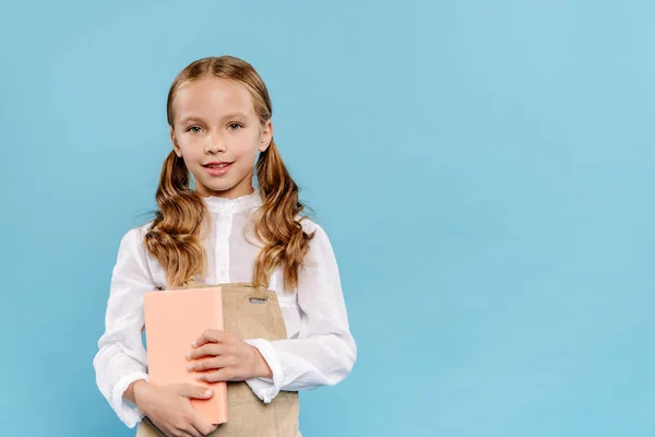 Smiling and cute kid looking at camera and holding book isolated on blue — Stock Photo