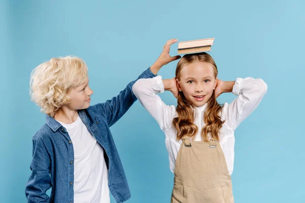 Boy putting book on head of his smiling friend isolated on blue — Stock Photo