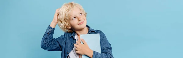 Panoramic shot of smiling and dreamy kid holding books isolated on blue — Stock Photo