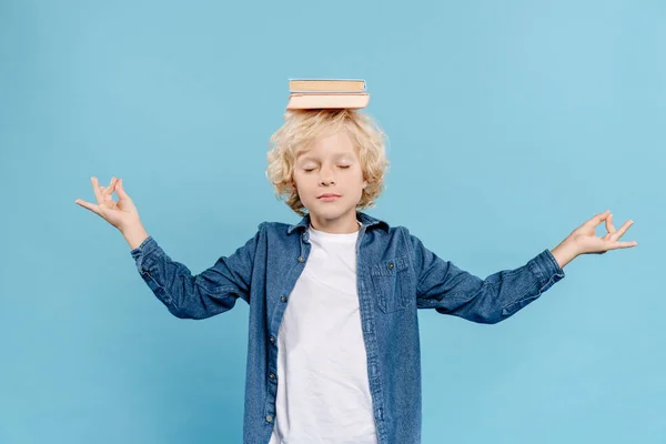 Cute kid with books on head meditating isolated on blue — Stock Photo