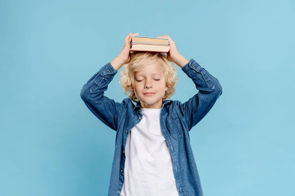 Nettes Kind mit geschlossenen Augen, das Bücher isoliert auf blauem Grund hält — Stockfoto