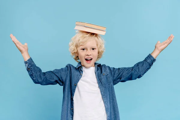 Smiling and cute with books on head looking at camera isolated on blue — Stock Photo