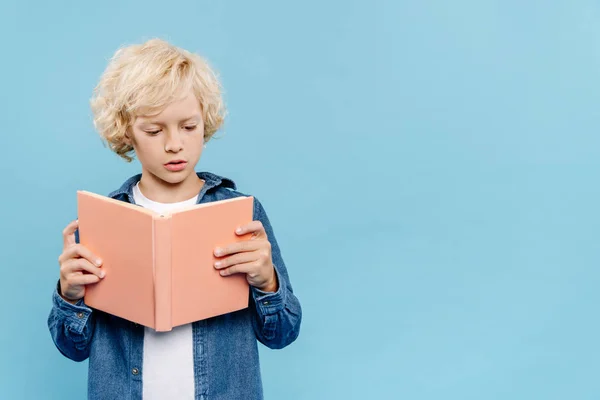 Rubio y lindo niño leyendo libro aislado en azul - foto de stock