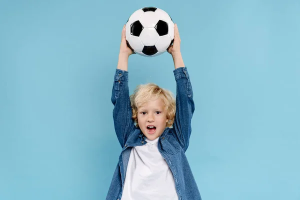 Lindo niño sosteniendo fútbol y gritando aislado en azul - foto de stock