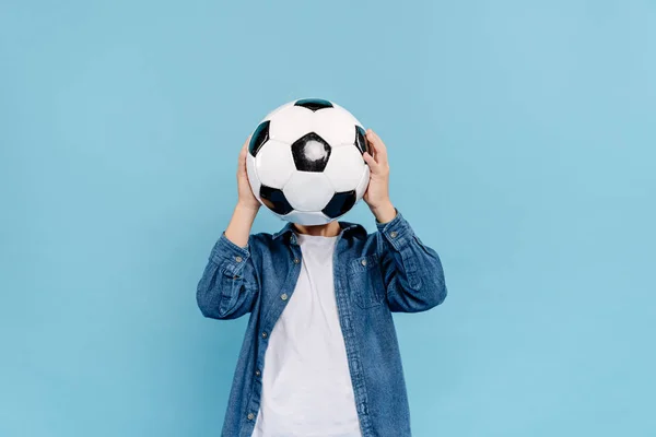 Kid obscuring face with football isolated on blue — Stock Photo