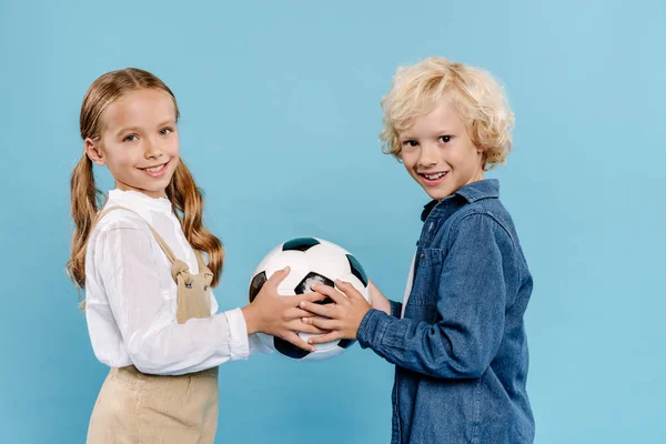Sonrientes y lindos niños sosteniendo fútbol aislado en azul - foto de stock