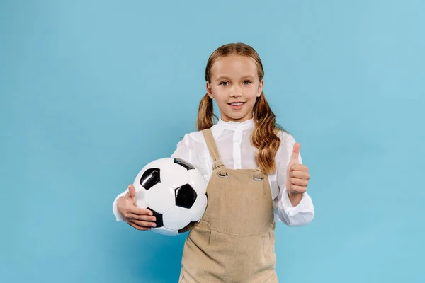 Lächelndes und nettes Kind, das wie Fußball auf blauem Hintergrund zeigt und hält — Stockfoto