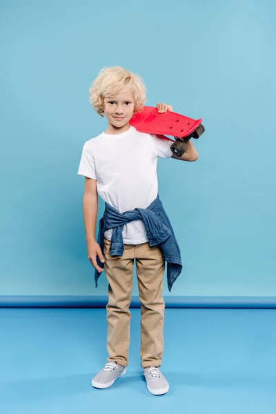Sorridente e carino bambino guardando la fotocamera e tenendo penny board su sfondo blu — Foto stock