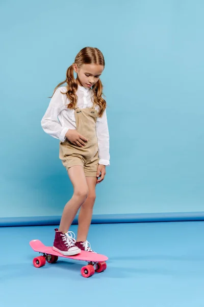 Carino bambino in piedi su penny board su sfondo blu — Foto stock