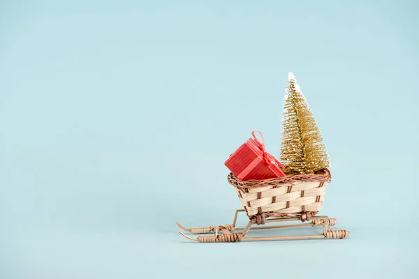 Traîneau en osier avec arbre de Noël et boîte cadeau sur fond bleu — Photo de stock