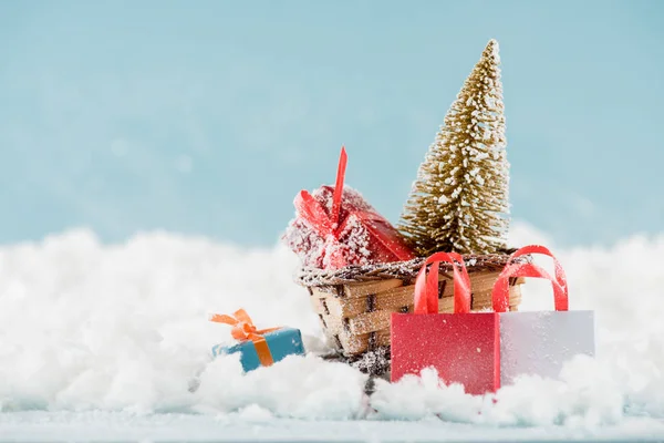 Подарункові коробки та різдвяна ялинка в плетених санчатах, сумки в снігу — стокове фото