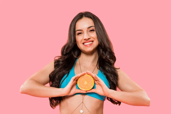 Счастливая девушка в купальнике держит половину оранжевого изолированы на розовый — стоковое фото