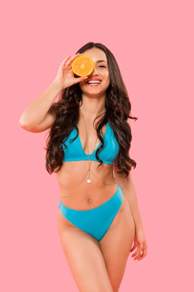 Sexy girl covering eye while holding half of orange isolated on pink — Stock Photo