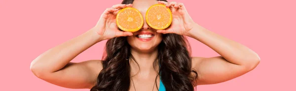 Panoramaaufnahme einer fröhlichen Frau, die ihr Gesicht verdeckt, während sie Orangen isoliert auf rosa hält — Stockfoto