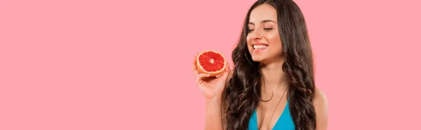 Панорамный снимок счастливой женщины, держащей половину грейпфрута изолированной на розовом — стоковое фото