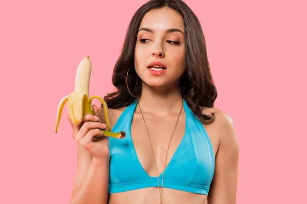 Beautiful young woman looking at peeled banana isolated on pink — Stock Photo