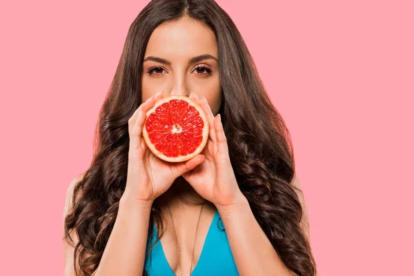 Young woman in swimsuit covering face with half of grapefruit isolated on pink — Stock Photo
