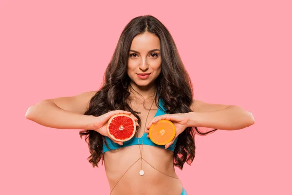 Atractiva mujer sosteniendo mitades de naranja y pomelo aislado en rosa - foto de stock