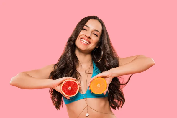 Mujer feliz sosteniendo mitades de naranja y pomelo aislado en rosa - foto de stock