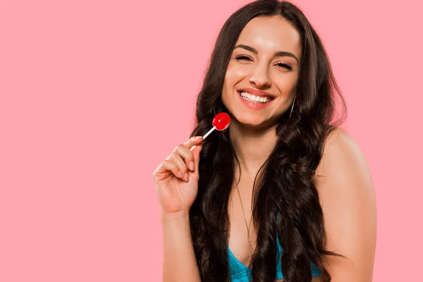 Mujer sonriente sosteniendo piruleta roja aislada en rosa - foto de stock