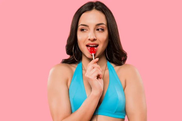 Pretty woman in swimsuit licking lollipop isolated on pink — Stock Photo