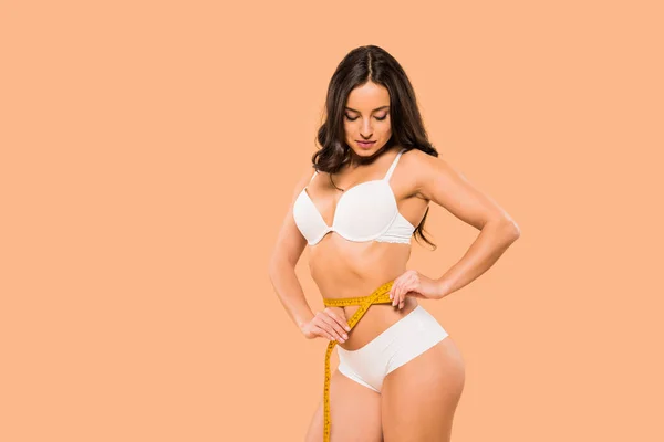 Beautiful woman in underwear measuring waist isolated on beige — Stock Photo