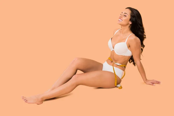 Beautiful woman in underwear smiling and sitting on beige — Stock Photo