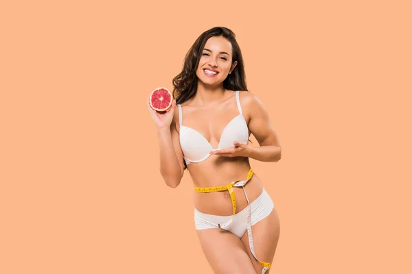 Cheerful woman in white underwear holding grapefruit isolated on beige — Stock Photo