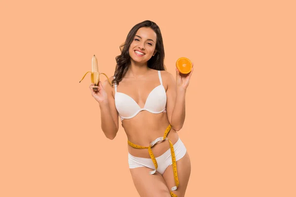 Fröhliche Frau hält Banane und Orange isoliert auf beige — Stockfoto