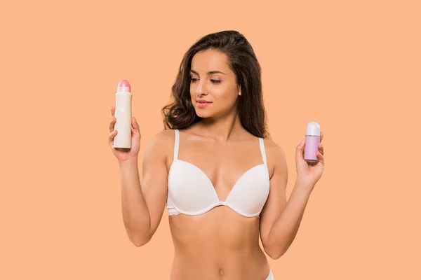 Atractiva mujer sosteniendo spray desodorante y rollo en aislado en beige - foto de stock