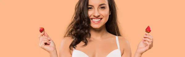 Panoramic shot of cheerful woman in white underwear holding red strawberries isolated on beige — Stock Photo