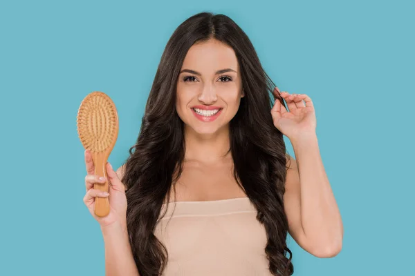 Glückliches Mädchen hält Haarbürste und berührt glänzendes Haar isoliert auf blau — Stockfoto
