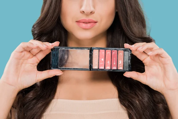 Vista recortada de la mujer sosteniendo paleta de brillo labial aislado en azul - foto de stock
