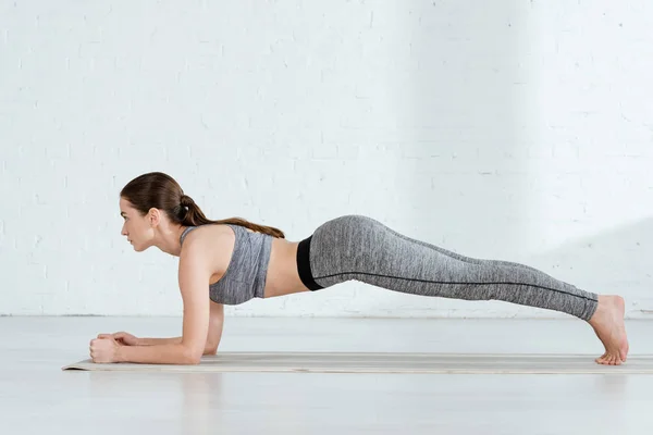 Side view of young woman in sportswear practicing yoga in forearm plank pose — Stock Photo