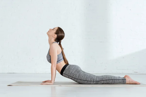 Vista laterale di giovane donna in abbigliamento sportivo praticare yoga in posa alto cobra — Foto stock