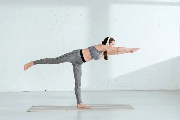 Junge Frau mit Kopfhörern praktiziert Yoga in Kriegerpose — Stockfoto