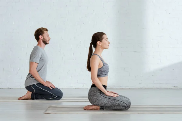 Vista lateral de joven hombre y mujer practicando yoga en pose de rayo - foto de stock