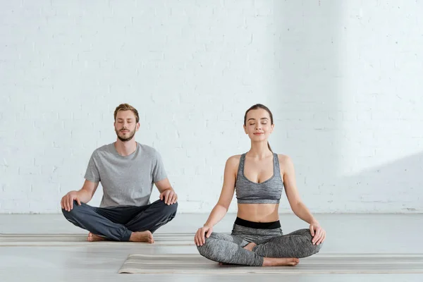 Joven hombre y mujer practicando yoga en pose de medio loto - foto de stock